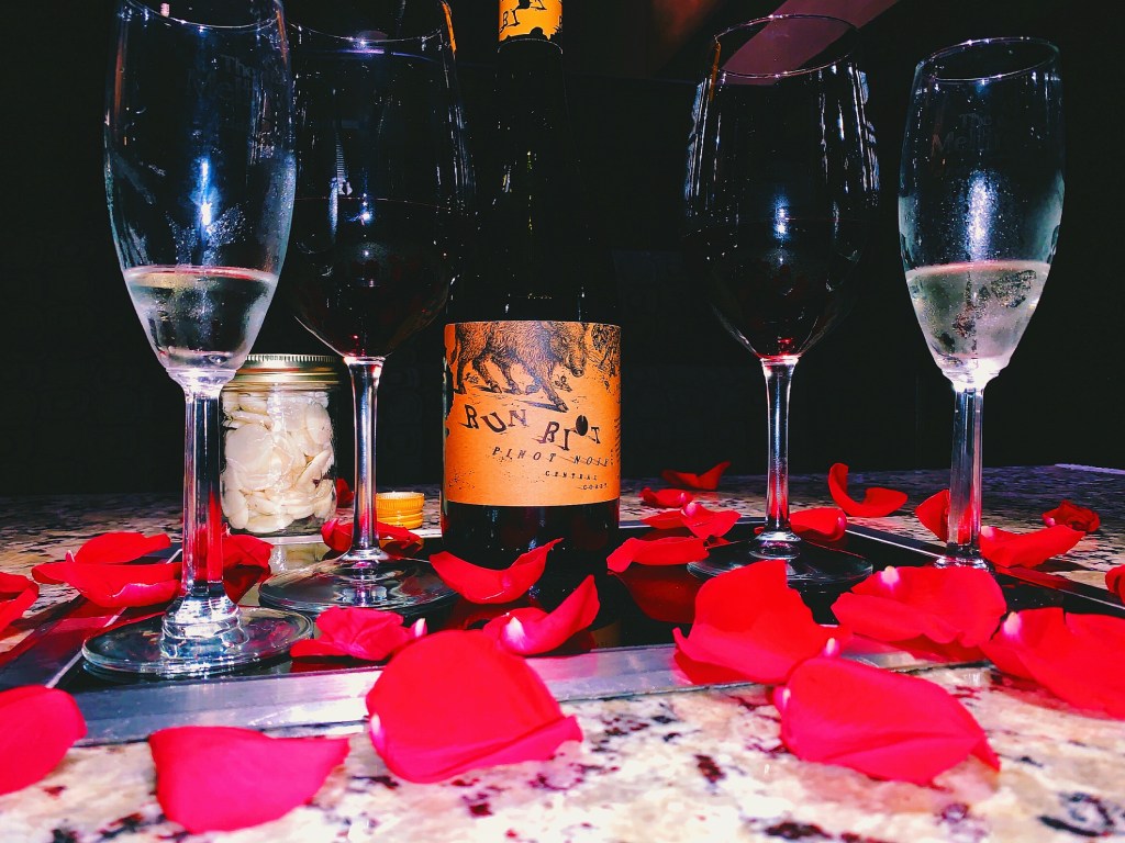 romantic table set for a special anniversary date with red rose pedals, wine glasses and a bottle of wine 